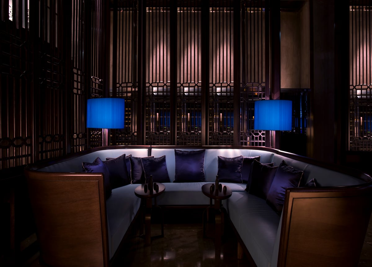 A curved booth at Hakkasan Abu Dhabi lit by blue lamps against dark lattice screens