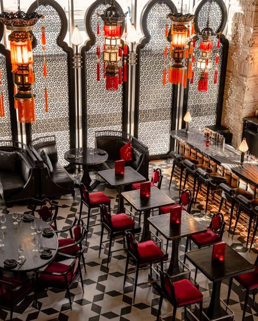 Red-cushioned chairs at small tables on a black and white tiled floor, red lanterns hanging along the bar