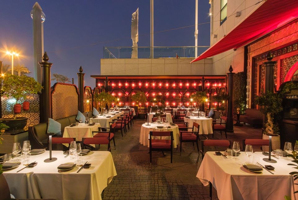 Laid tables on the terrace at night, a wall of red lanterns behind