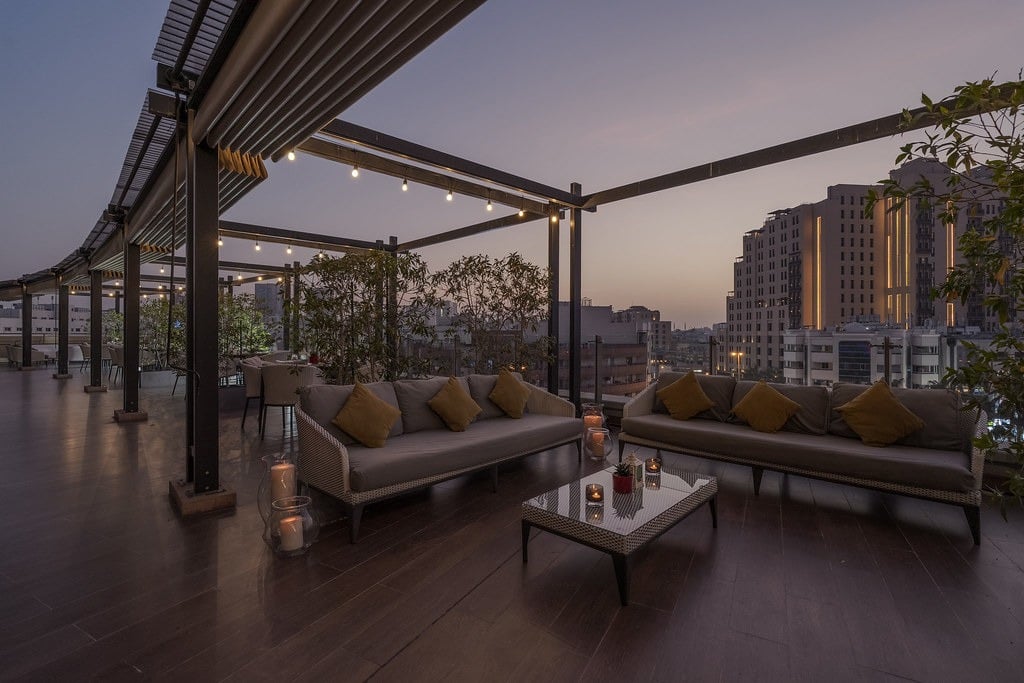Sofas and a low table on a timber-decked terrace under a pergola, the Deira skyline at dusk
