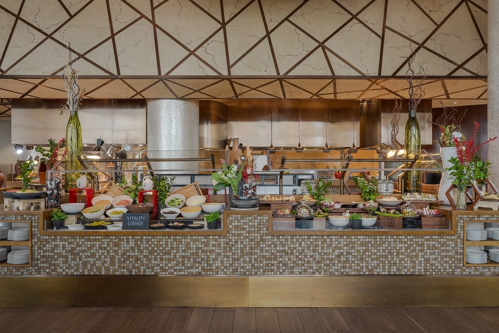 A long mosaic buffet counter laden with salads and dishes beneath an angular lattice ceiling