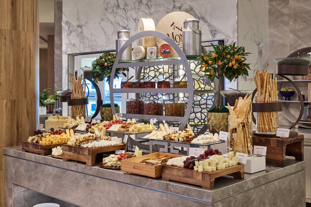 Wheels and wedges of cheese with breads and crackers arranged on a marble counter under a brass stand