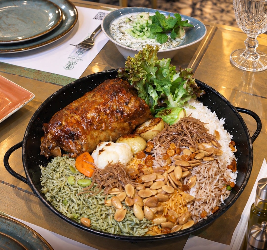 Roast lamb on a pan of herbed and vermicelli rice with almonds and raisins, a yoghurt and cucumber dip behind