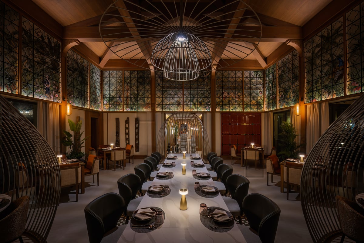 Tables laid under a carved timber ceiling, latticed windows glowing on every side