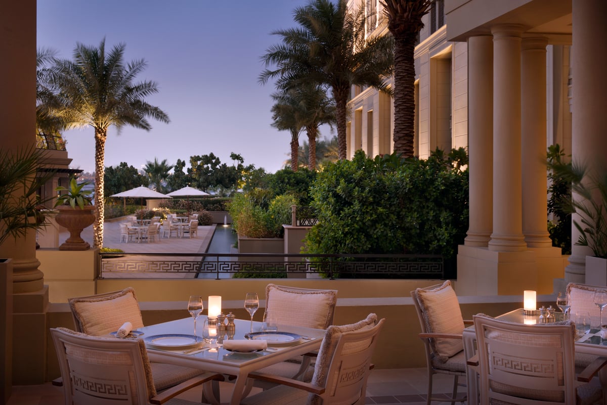 Candlelit tables on a colonnaded terrace overlooking palms and the hotel gardens at dusk