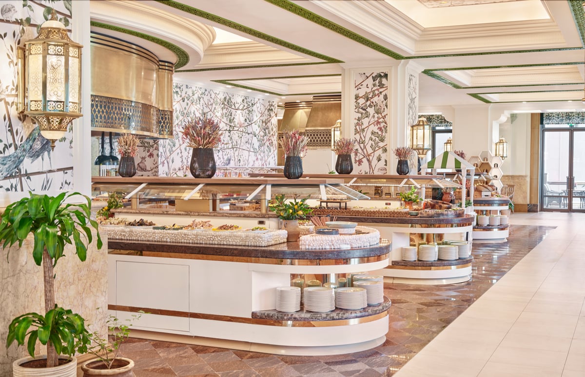 Curved white buffet counters on a patterned floor, botanical murals and brass lanterns on the walls