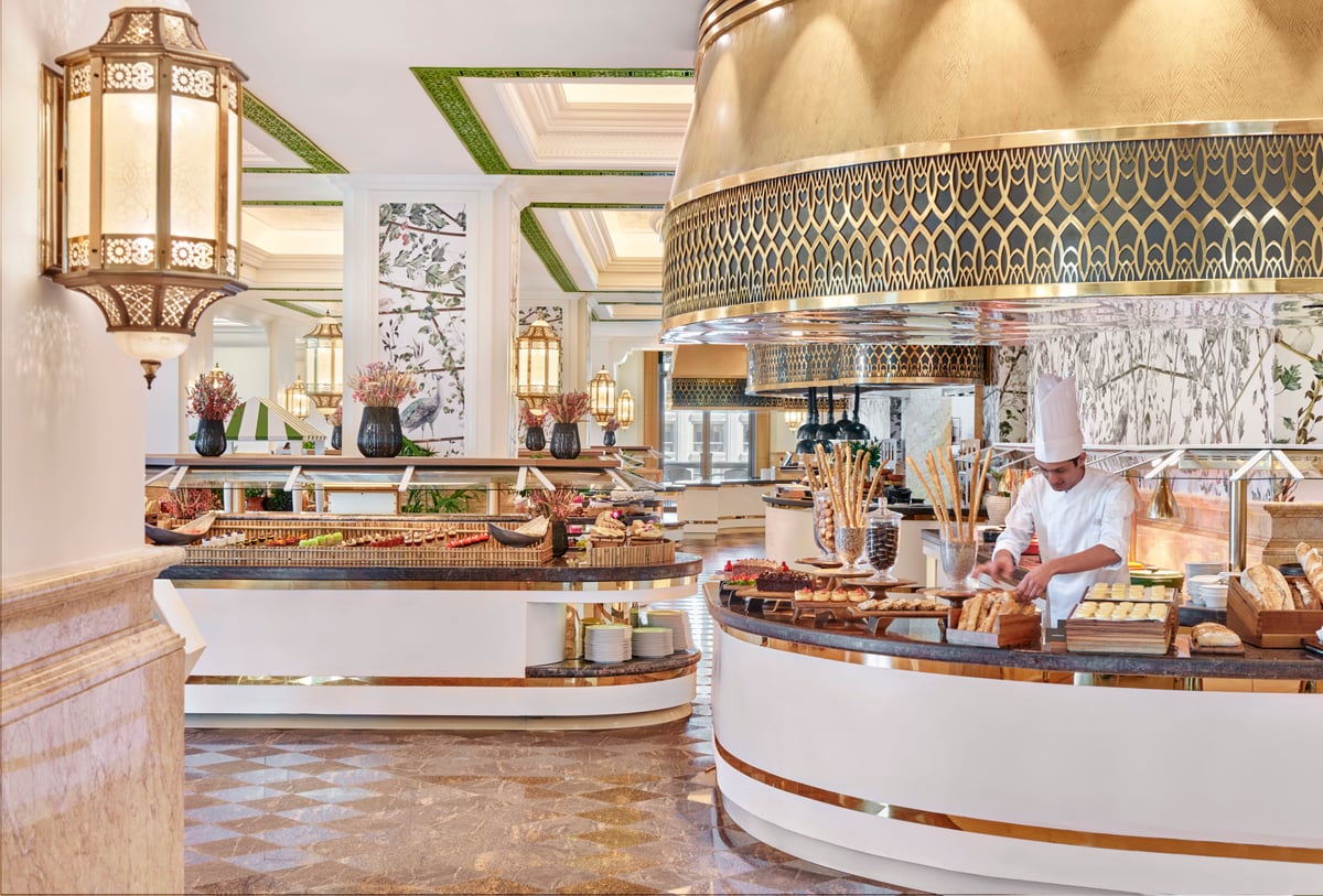 A chef at a curved counter of breads and pastries beneath a gilded lattice hood